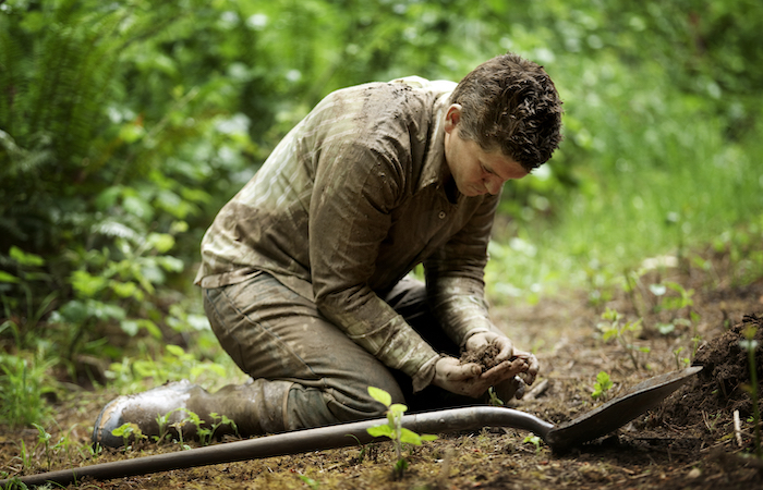 farmer searching for mud in a forest with hands and shovel
