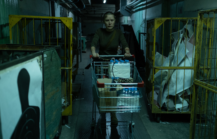 woman in post apocalypse pushing a shopping cart with water bottles