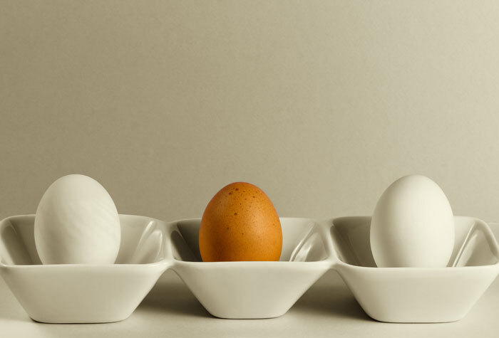 Two white duck eggs and one brown chicken egg standing upright in a tray.