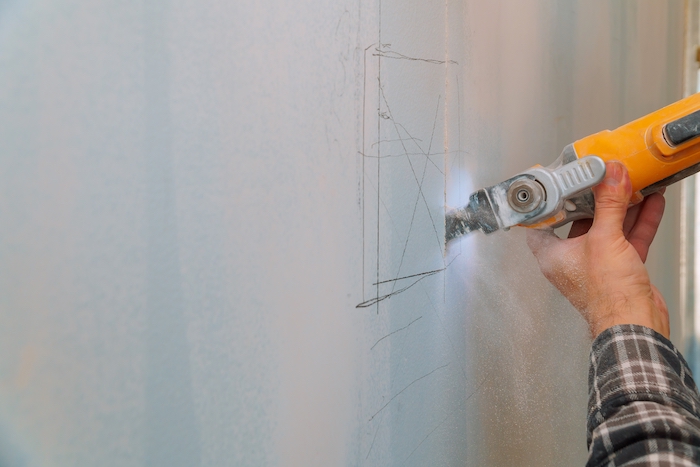 hand holding saw cutting into a wall