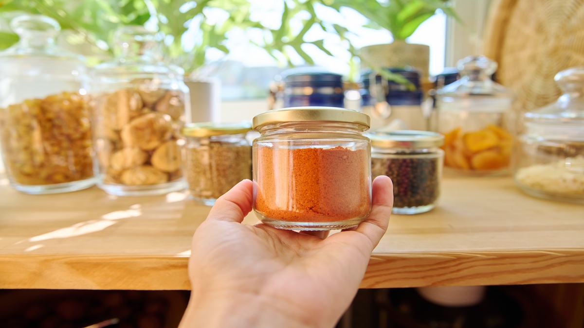 Hand holding a jar filled with paprika and surrounded by other spice jars.
