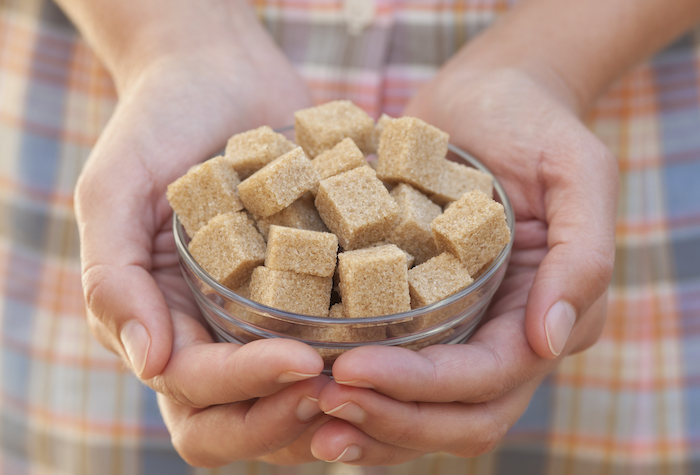 Woman holding a bowl of brown sugar cubes in her hands.