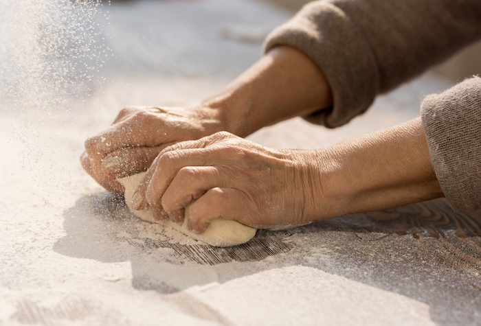 Hands of mature female kneading dough in flour on wooden table before making baking homemade pastry.