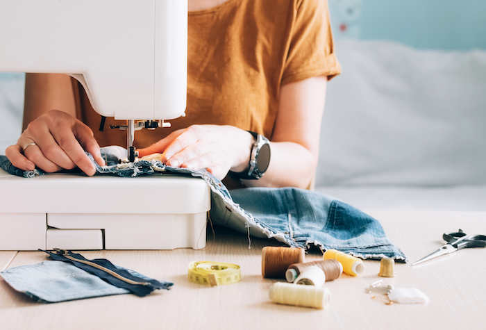 A woman tailor works at a sewing machine sews reuses fabric from old denim clothes.