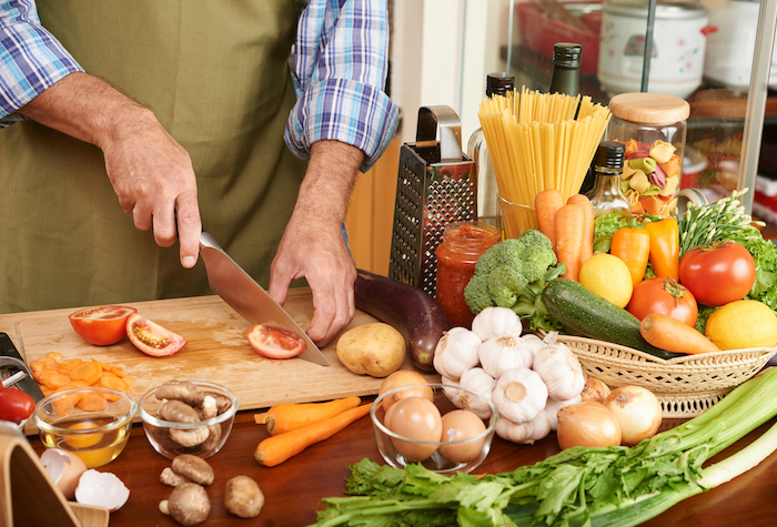 Man chopping tomatoes on a wooden cutting board surrounded by other vegetables and ingredients.