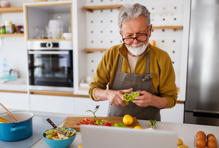 Man cooking in home kitchen cutting a pepper with other vegetables on a wooden cutting board.