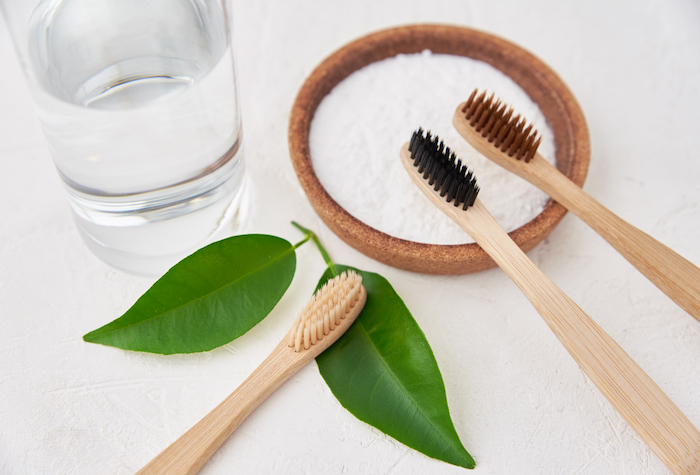 Bowl of Baking soda with three toothbrushes and a glass of water.