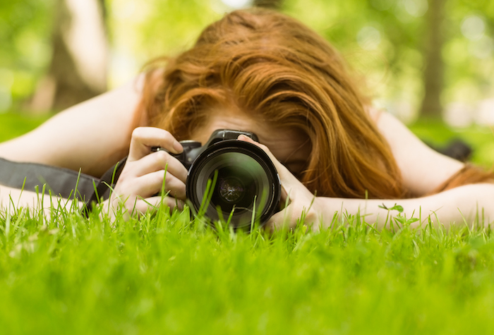 Close up of female photographer lying in the grass taking a photo.