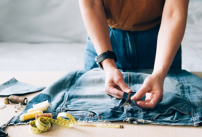 Woman is leaning over an old pair of blue jeans that she is cutting and repurposing. 