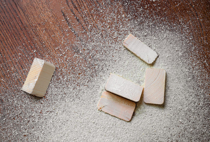 Closeup of cut pieces of wood with sawdust on brown wooden floor.