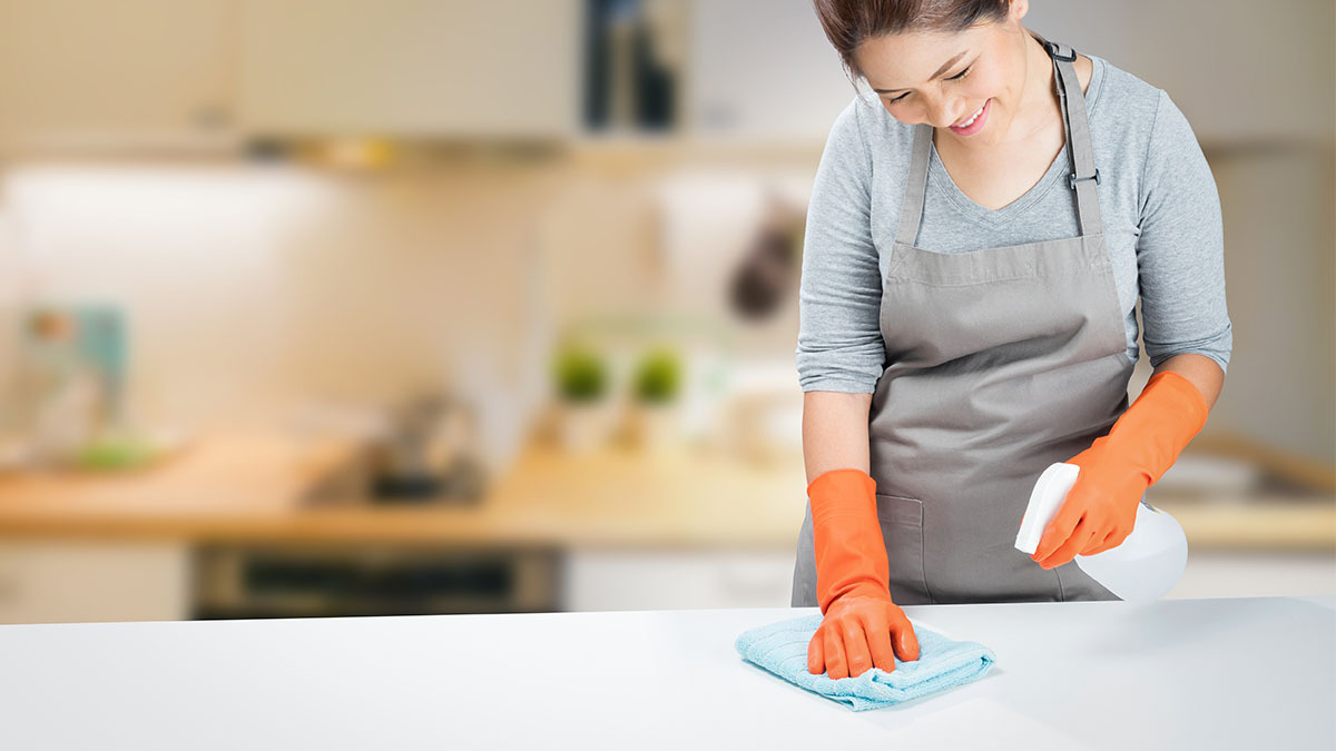 Woman spraying a kitchen counter with cleaner.