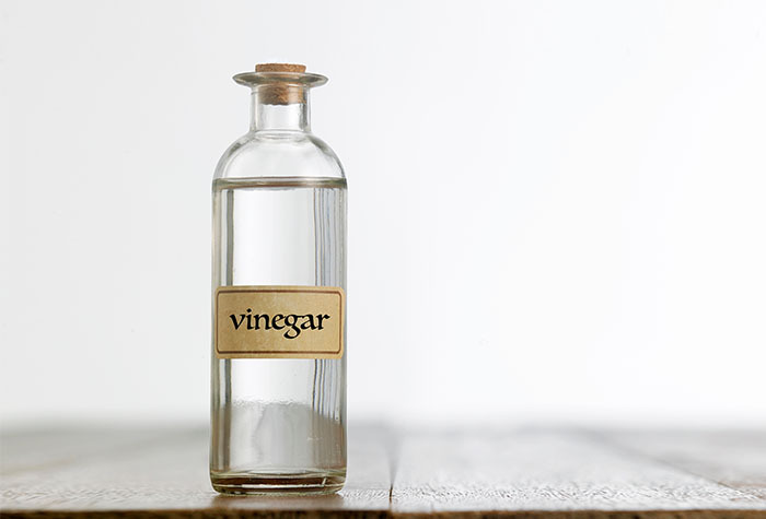 Glass bottle of vinegar sitting on a table.