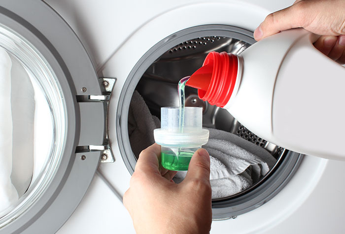 Person pouring cleaning laundry detergent into a laundry cup.