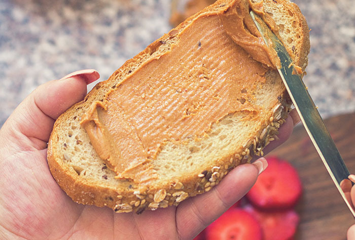 Woman slathering peanut butter on a slice of bread. 