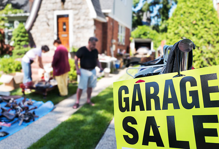 A garage sale happening on someones front lawn with goods laid out.