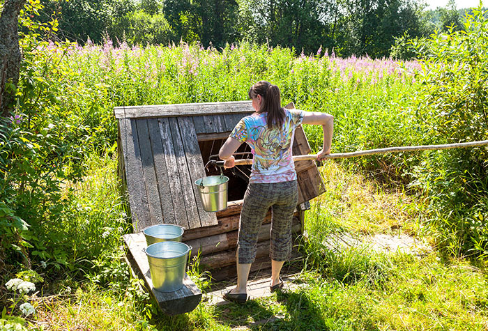 Woman drawing pails of water from her at-home well for a more self-sufficient lifestyle.