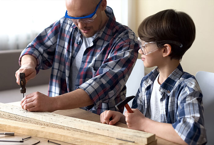 A young boy in a workshop with his dad learning how to use tools.