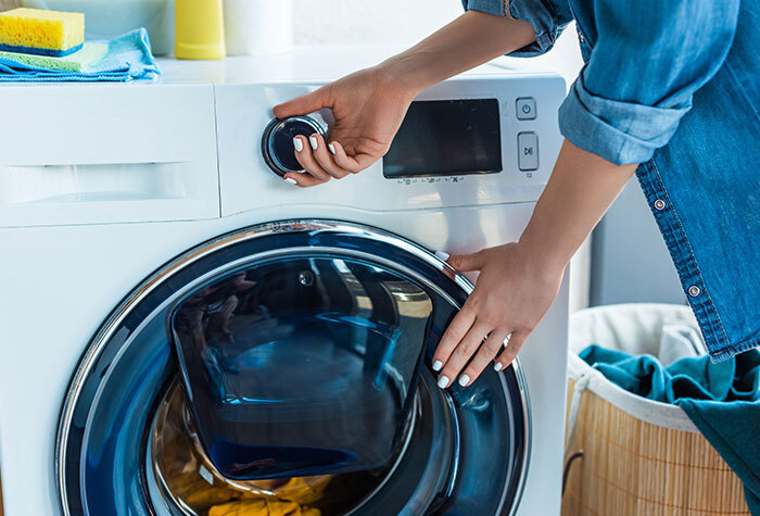 A woman starting a load of clothes in the washing machine.