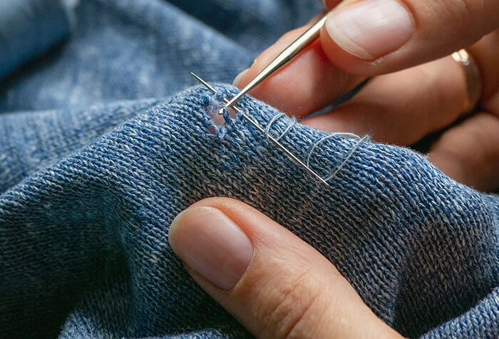 Someone mending a sweater with a needle and thread.