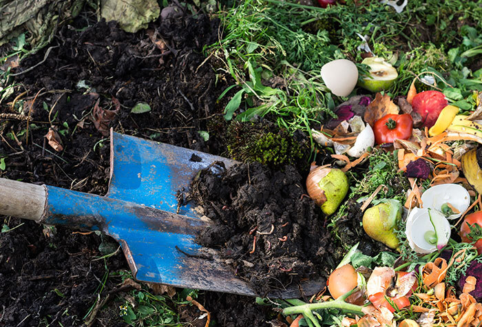 A person turning their compost pile in the springtime with a shovel.