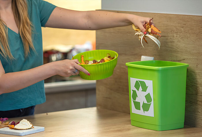 A person dropping scraps into their kitchen compost bin.