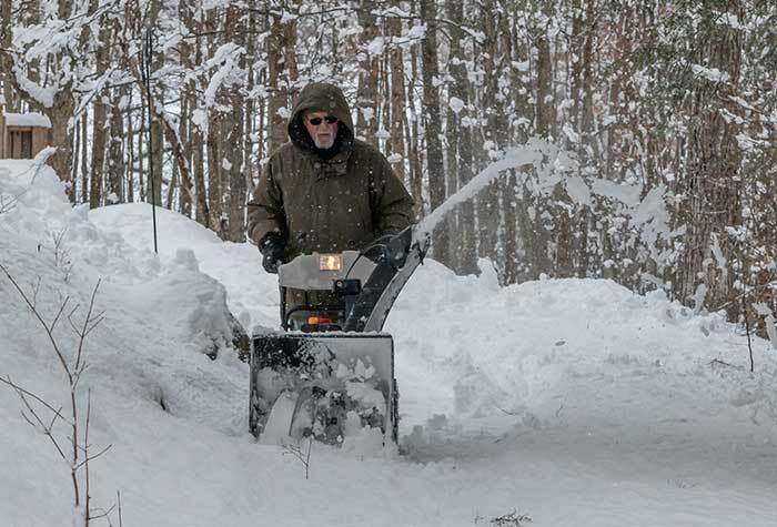 A man using his snowblower to forge a path through the snow on his homestead.