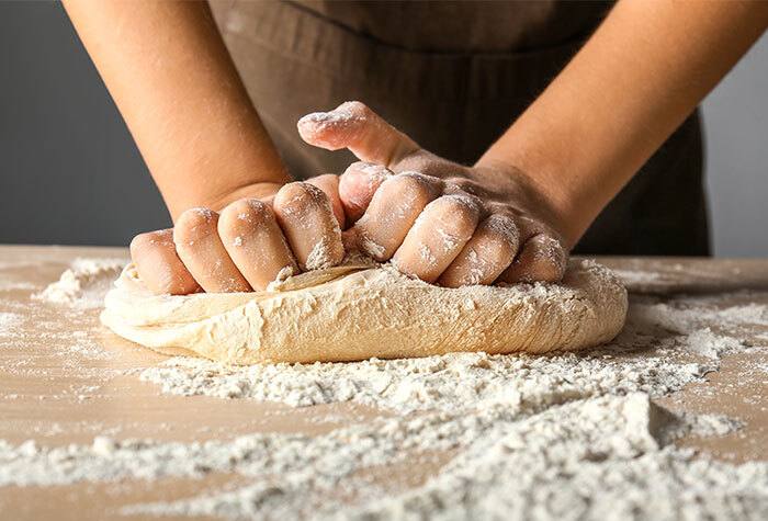 A person kneading bread dough on a floured surface.