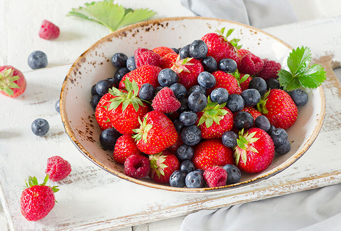 A white bowl on a white cutting board filled with strawberries, raspberries, and blueberries.