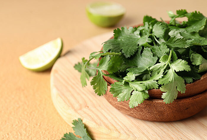 A bowl of fresh, green cilantro in a wooden bowl, on a wooden cutting board next to a lime slice.