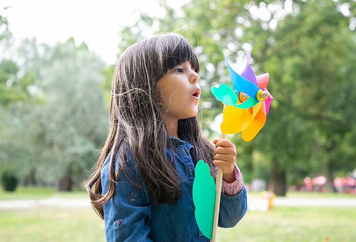 A young girl blowing on a colorful pinwheel.